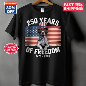 May include: A black t-shirt featuring a graphic of a dog wearing a red, white, and blue top hat and bandana in front of an American flag. The text reads 250 YEARS OF FREEDOM 1776 - 2026 in white lettering above and below the dog illustration.