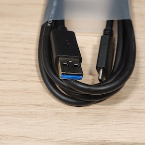 May include: A black USB-C to USB-A cable coiled up with the USB-A connector visible. The cable is packaged in a clear plastic bag with a label that says "Google Pixel" and has a QR code.