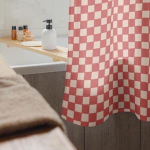 May include: A red and white checkered shower curtain hangs in a bathroom. A wooden bath tray holds a white soap dispenser, small bottles, and a brush. A beige towel is in the foreground.
