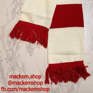 May include: A red and white striped scarf with fringed ends. The scarf is made of a soft material and has alternating bands of red and white. The scarf is displayed on a marble surface.