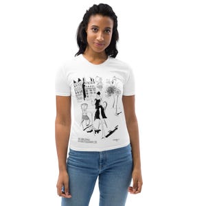 May include: White t-shirt with a black and white illustration of a woman sitting at a cafe table in front of a building. The text "Rue Saint-Andre des Arts" is printed on the shirt.