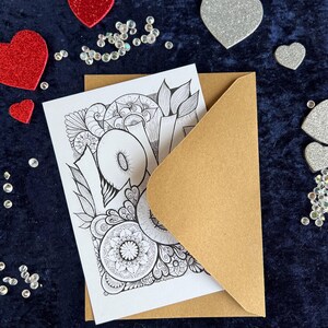 Handgezeichnete Love Postkarte zum Ausmalen mit Mandala- und floralen Mustern und braunem Briefumschlag auf dunklem Stoff dekoriert mit Herz Deko
