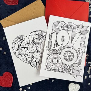 2 Love Postkarten selbst gemalt mit zentangle und Mandala Muster zum Ausmalen. Zwei Briefumschläge in rot und braun liegen im Hintergrund. Herz Deko drumherum