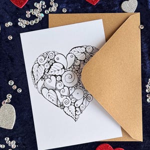 Herz Postkarte mit Zentangle Muster mit dem Wort Love in der Mitte mit braunem Briefumschlag und Deko im Hintergrund