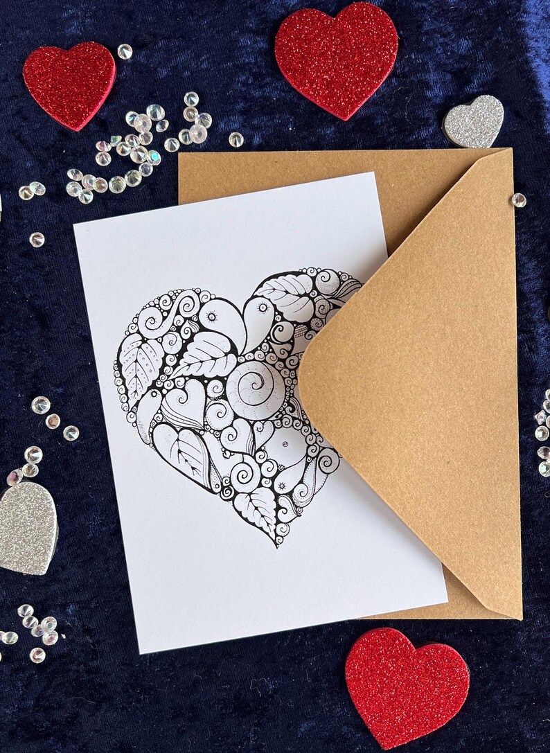 Herz Postkarte mit Zentangle Muster mit dem Wort Love in der Mitte mit braunem Briefumschlag und Deko im Hintergrund