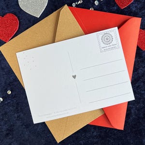 Rückseite der love Postkarte mit zwei Briefumschlägen in braun und rot auf einer blauen Decke liegend mit Herz Deko drumherum