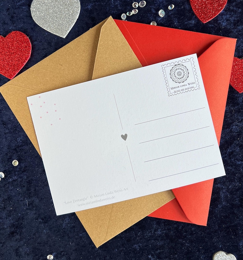 Rückseite der love Postkarte mit zwei Briefumschlägen in braun und rot auf einer blauen Decke liegend mit Herz Deko drumherum