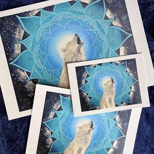 Wolf Krafttier Bild "Der Ruf". Drei Gicleé Drucke in drei verschiedenen Größen. Zu sehen ist ein weißer Wolf, der ruft, umgeben von einem Mandala in blau-Tönen. Das Original Bild wurde gemalt von der Künstlerin Miriam Linda Weiss.
