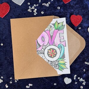 Handgezeichnete Love Postkarte zum Ausmalen (mit Buntstiften angemalt) und braunem Briefumschlag auf dunklem Stoff dekoriert mit Herz Deko