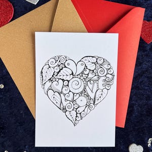 Herz Postkarte zum Ausmalen in Schwarz-Weiß mit filigranem Herzmotiv auf weißem Hintergrund. Zentangle Muster mit dem Wort Love in der Mitte. Zwei Briefumschläge in rot und braun liegen im Hintergrund