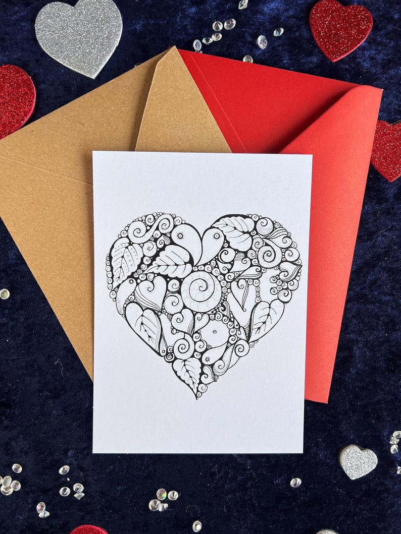 Herz Postkarte zum Ausmalen in Schwarz-Weiß mit filigranem Herzmotiv auf weißem Hintergrund. Zentangle Muster mit dem Wort Love in der Mitte. Zwei Briefumschläge in rot und braun liegen im Hintergrund