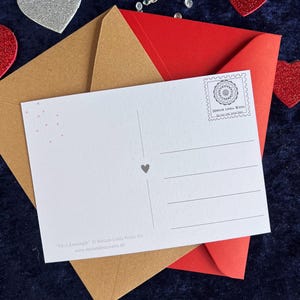 Rückseite der Herz Postkarte zum Ausmalen. Im Hintergrund liegen zwei Briefumschläge in braun und rot und Deko