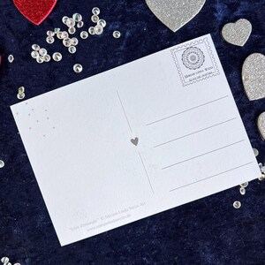 Rückseite der love Postkarte auf einer blauen Decke liegend mit Herz Deko drumherum
