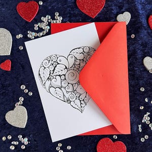 Herz Postkarte mit Zentangle Muster mit dem Wort Love in der Mitte mit rotem Briefumschlag und Deko im Hintergrund