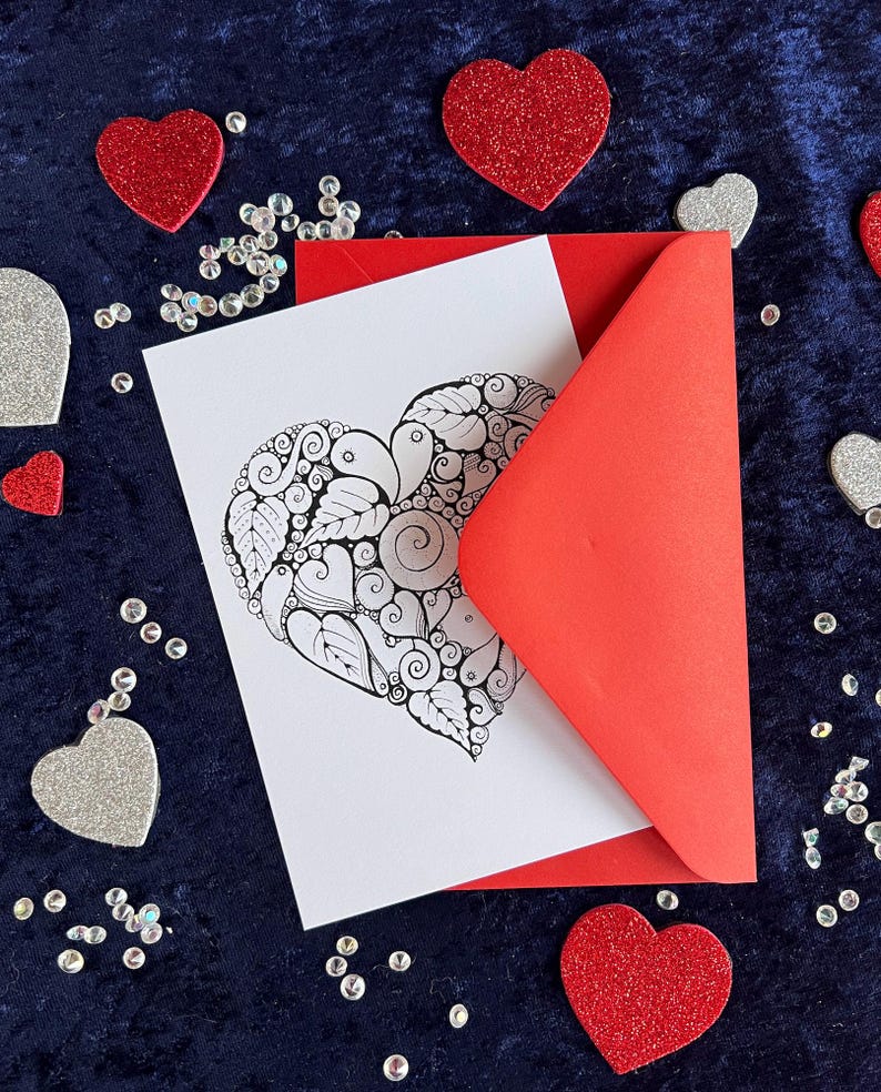 Herz Postkarte mit Zentangle Muster mit dem Wort Love in der Mitte mit rotem Briefumschlag und Deko im Hintergrund