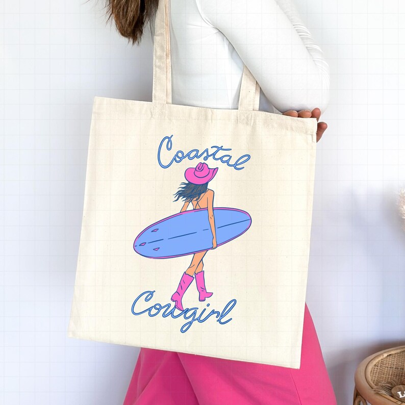 May include: A white canvas tote bag with a pink and blue illustration of a woman wearing a cowboy hat and boots, holding a surfboard. The text "Coastal Cowgirl" is printed on the bag.