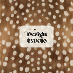 May include: A brown and white spotted pattern background with a cream-colored rectangular label. The label features the text "DAFNE + Design Studio +" in a black, stylized font. The overall design has a natural, organic feel.