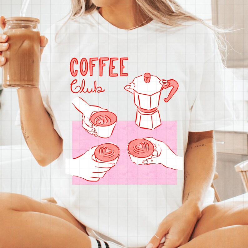 May include: White t-shirt with a pink graphic featuring coffee-related illustrations and the words "COFFEE Club" in red. The graphic includes a coffee maker, hands holding cups of coffee, and latte art.