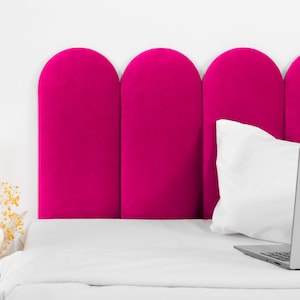 Puede incluir: Un cabecero fucsia vibrante con un diseño arqueado, sobre una pared blanca. Una almohada blanca y un portátil plateado están en la cama. La cama está cubierta con una sábana blanca. Flores secas a la izquierda.