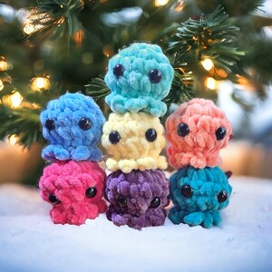 May include: A stack of seven crocheted octopus plushies in various colours, including blue, yellow, pink, purple, and teal. The plushies are arranged in a pyramid shape, with the largest at the bottom and the smallest at the top.