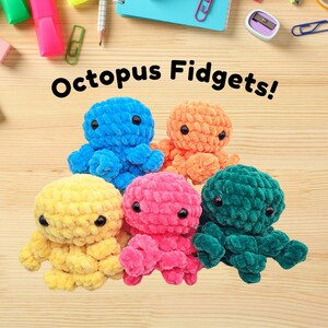 May include: Five crocheted octopus plushies in different colours: yellow, blue, orange, pink, and green. The plushies are arranged in a semi-circle on a wooden surface. The text "Octopus Fidgets!" is written above the plushies.