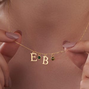 May include: Gold necklace with three initial charms, 'E', 'B', and a green gemstone.