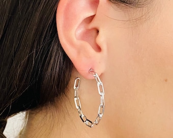 May include: Silver chain link hoop earrings. The earrings are worn in a person's ear.