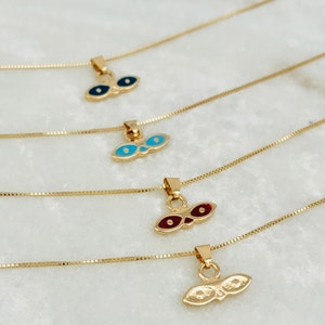 May include: Four gold necklaces with different colored eye pendants. The pendants are shaped like a pair of eyes with a gold frame. The necklaces are on a white surface.