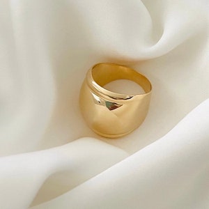 May include: A gold-toned ring with a rounded, domed design. The ring is thick and has a smooth, polished finish.