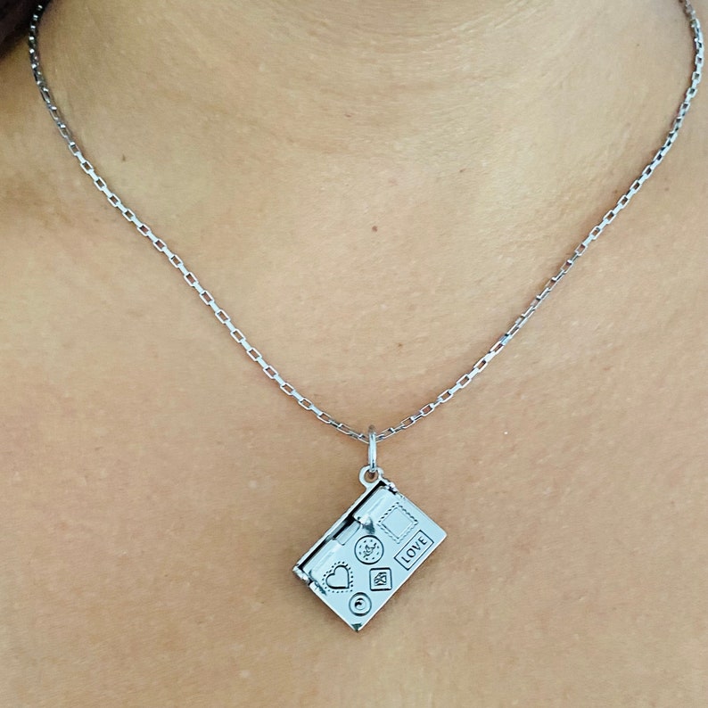 May include: A silver chain necklace with a silver charm pendant shaped like a closed envelope with a heart, a star, and a circle on the front. The envelope has the word "LOVE" printed on it.