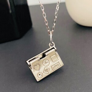 May include: Silver necklace with a charm that looks like a small book with a heart, a flower, a diamond, a square, and the word "LOVE" engraved on it.
