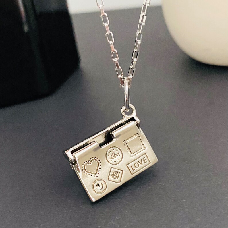 May include: Silver necklace with a charm that looks like a small book with a heart, a flower, a diamond, a square, and the word "LOVE" engraved on it.