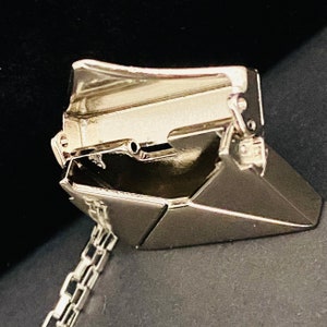 May include: A silver-toned metal necklace with a detailed, hinged, and foldable pendant shaped like a briefcase. The pendant is open and the chain is visible.