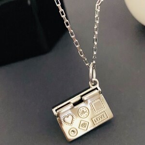 May include: A silver necklace with a small silver charm that opens to reveal a heart, a circle, a diamond, a star, and a square with the word "LOVE" engraved on it.