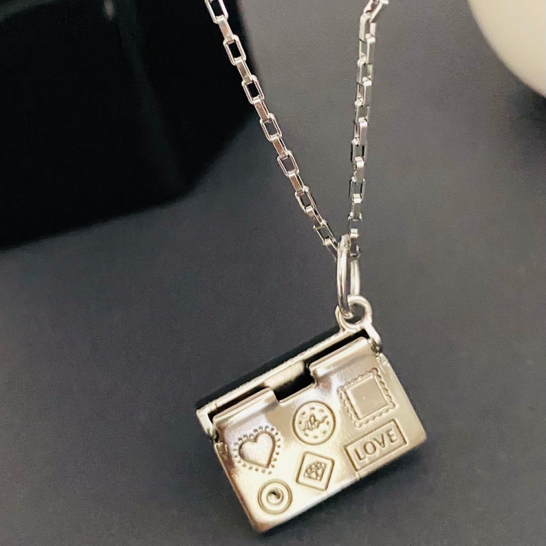 May include: A silver necklace with a small silver charm that opens to reveal a heart, a circle, a diamond, a star, and a square with the word "LOVE" engraved on it.