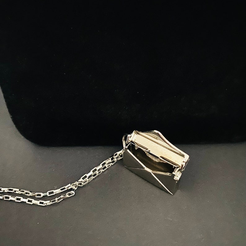 May include: A silver necklace with a silver envelope pendant. The envelope is open and has a silver chain inside.