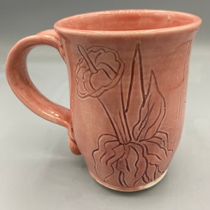 May include: A pink ceramic mug with a floral design. The mug has a handle and a wide mouth.