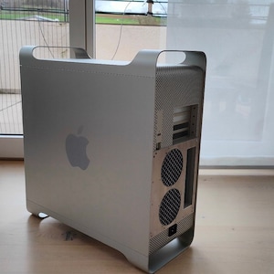 Könnte beinhalten: Ein silberner Apple Power Mac G5 Computerturm mit einem Gehäuse aus gebürstetem Aluminium, integrierten Tragegriffen oben und einem Apple-Logo auf der Seite. Die Rückseite zeigt zwei runde Lüftergitter sowie diverse Anschlussmöglichkeiten.