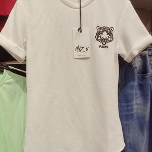 Puede incluir: Camiseta blanca de manga corta con un gráfico de tigre negro y el texto "MIZ-U PARIS" en una etiqueta blanca.