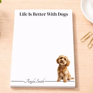May include: A rectangular white notepad featuring the black text Life Is Better With Dogs at the top, a brown curly-haired dog illustration in the bottom right corner, and the name Angela Smith printed in black script above a horizontal line.
