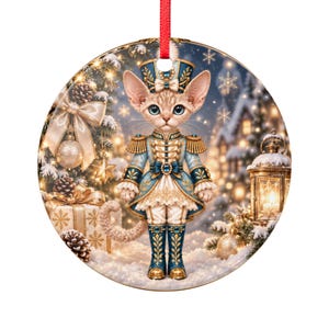 Può includere: Un ornamento rotondo in ceramica raffigurante un gatto vestito da schiaccianoci con un'uniforme blu e oro e un cappello abbinato. Lo sfondo mostra una scena invernale innevata con un albero di Natale decorato, regali e una lanterna.