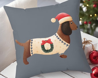 May include: A gray throw pillow with a festive dachshund wearing a Santa hat and a sweater with a wreath. The dachshund is brown with a white sweater and a red bow.