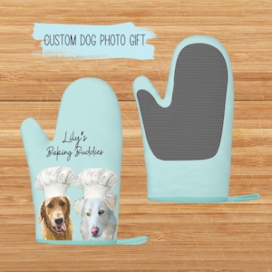 May include: A pair of blue oven mitts with a gray heat-resistant lining. The mitts feature a personalized design with two dogs wearing chef hats and the text "Lily's Baking Buddies".