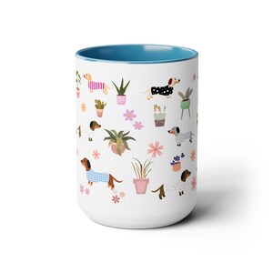 May include: White ceramic mug with a blue rim featuring a repeating pattern of dachshunds wearing pajamas and potted plants. The dachshunds are in various colors and patterns.
