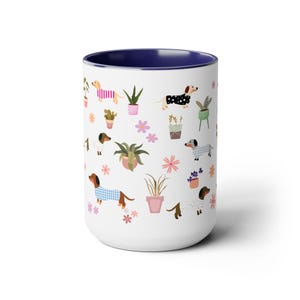 May include: White ceramic mug with a blue rim featuring a repeating pattern of dachshunds wearing pajamas and potted plants. The dachshunds are brown, black, and white.