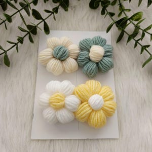 May include: Four crocheted flower hair clips in yellow, white and green. The flowers are layered with two colours.