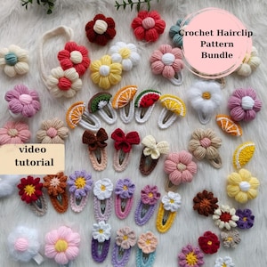 Könnte beinhalten: Eine Sammlung von gehäkelten Haarklammern in verschiedenen Farben und Designs, darunter Blumen, Früchte und Schleifen. Die Klammern sind auf einer weißen Oberfläche angeordnet, auf der der Text "Crochet Hairclip Pattern Bundle" und "video tutorial" zu sehen ist.