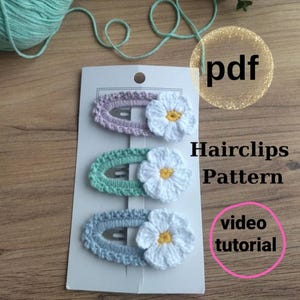 May include: Three crochet hair clips in pastel colors: lavender, mint green, and light blue. Each clip features a white daisy with a yellow center. The image includes the text "Hairclips Pattern" and "video tutorial".