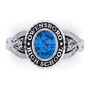 May include: A silver ring with a blue oval stone and two smaller diamond-shaped stones on either side. The ring has a black band with the words "Owensboro High School" inscribed around the stone.