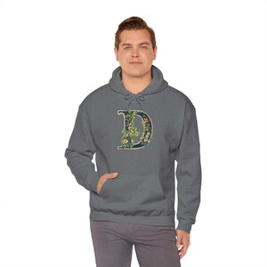 Könnte beinhalten: Ein dunkelgrauer Kapuzenpullover mit einem floralen Design, das den Buchstaben "D" in Marineblau zeigt.